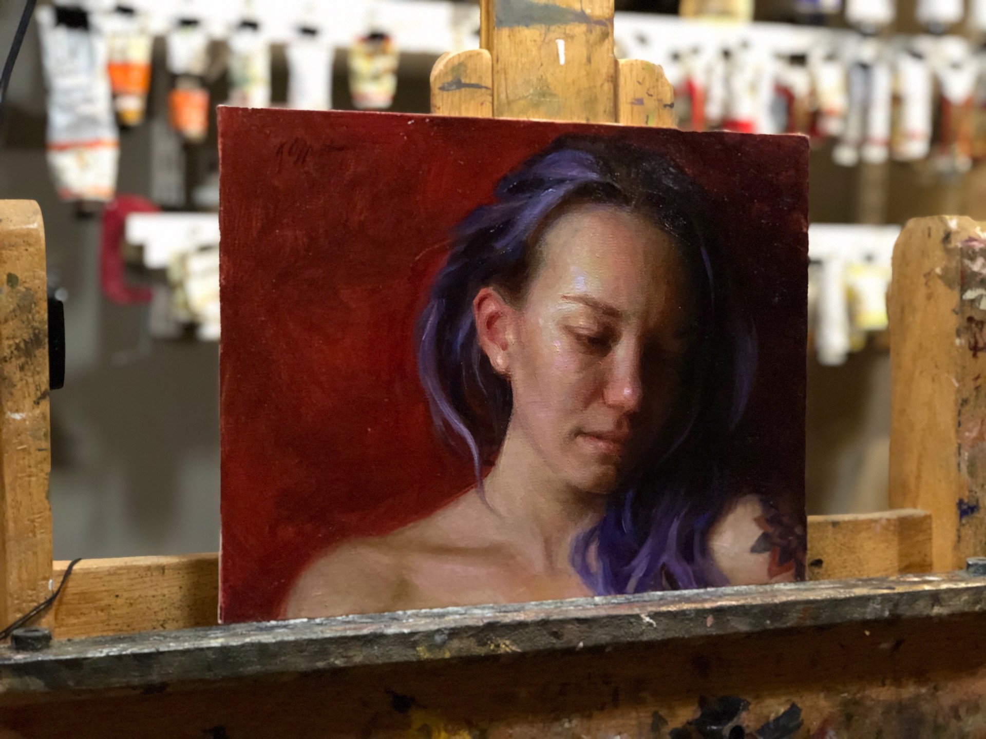 A portrait of a person with purple hair and a visible tattoo, set against a deep red background.