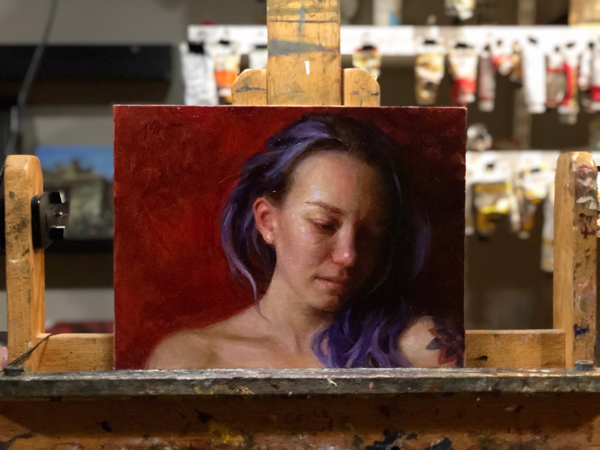 A portrait of a person with purple hair and a visible tattoo, set against a deep red background.