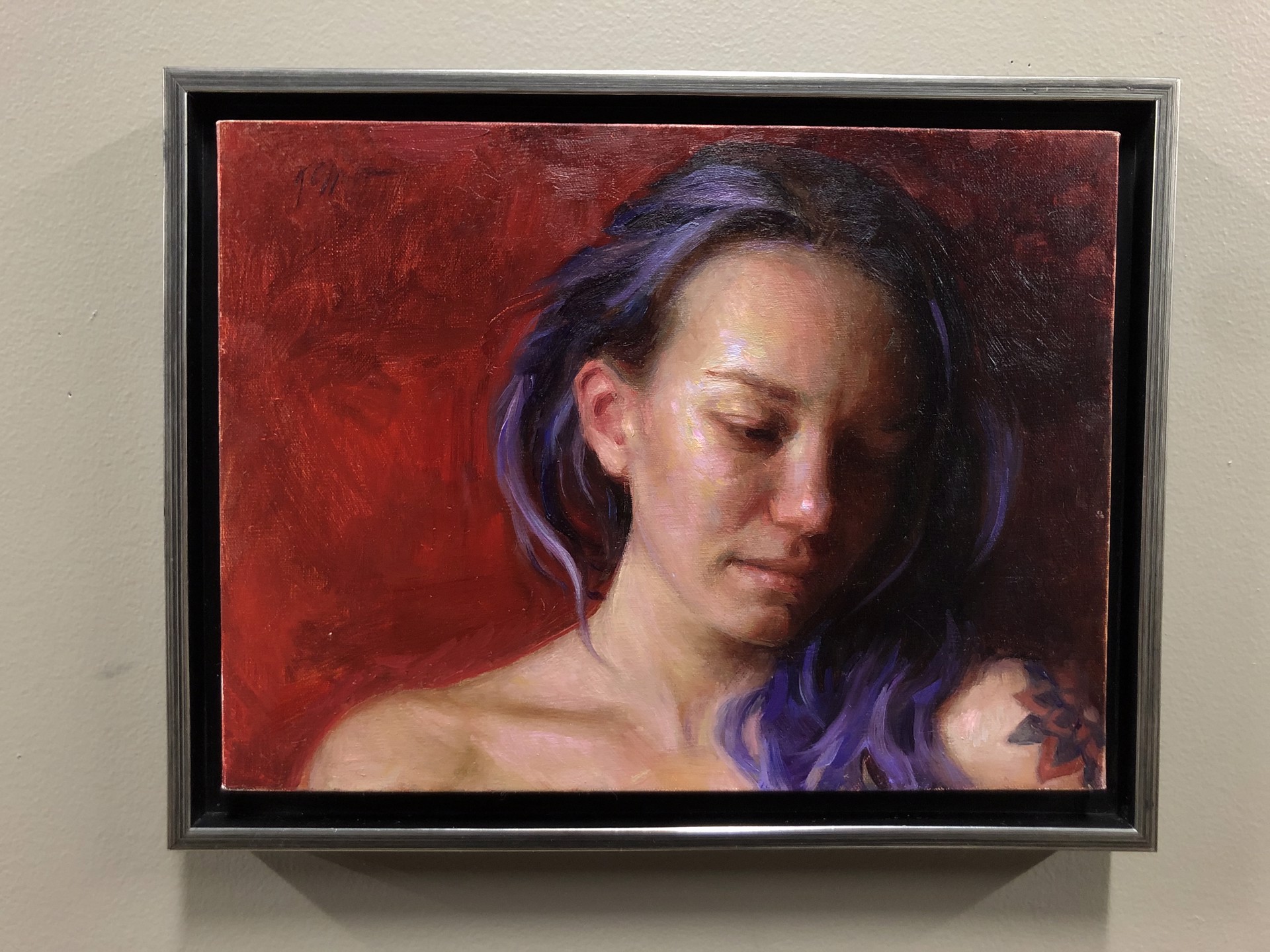 A portrait of a person with purple hair and a visible tattoo, set against a deep red background.