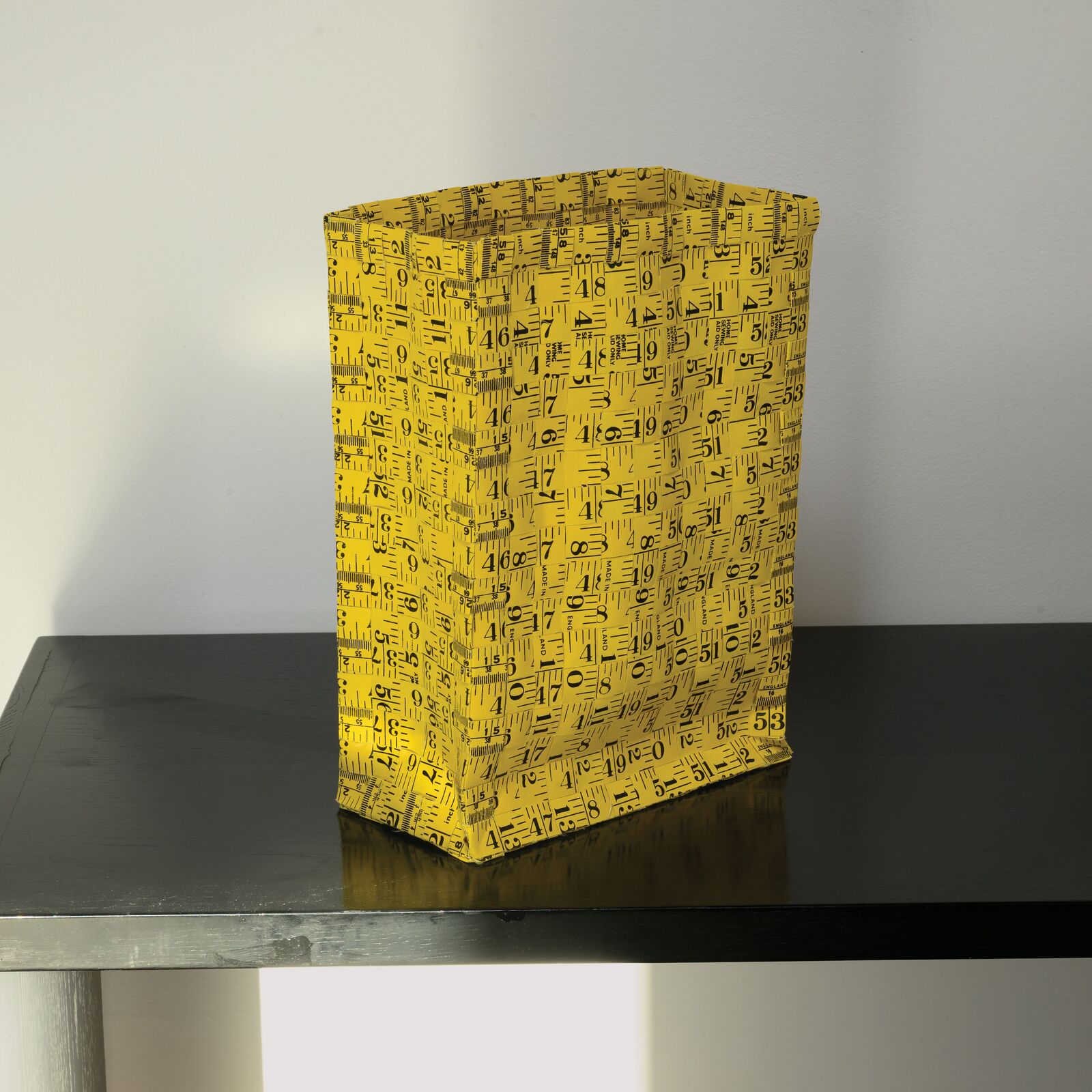 A yellow gift bag with a black geometric pattern sits on a dark table.
