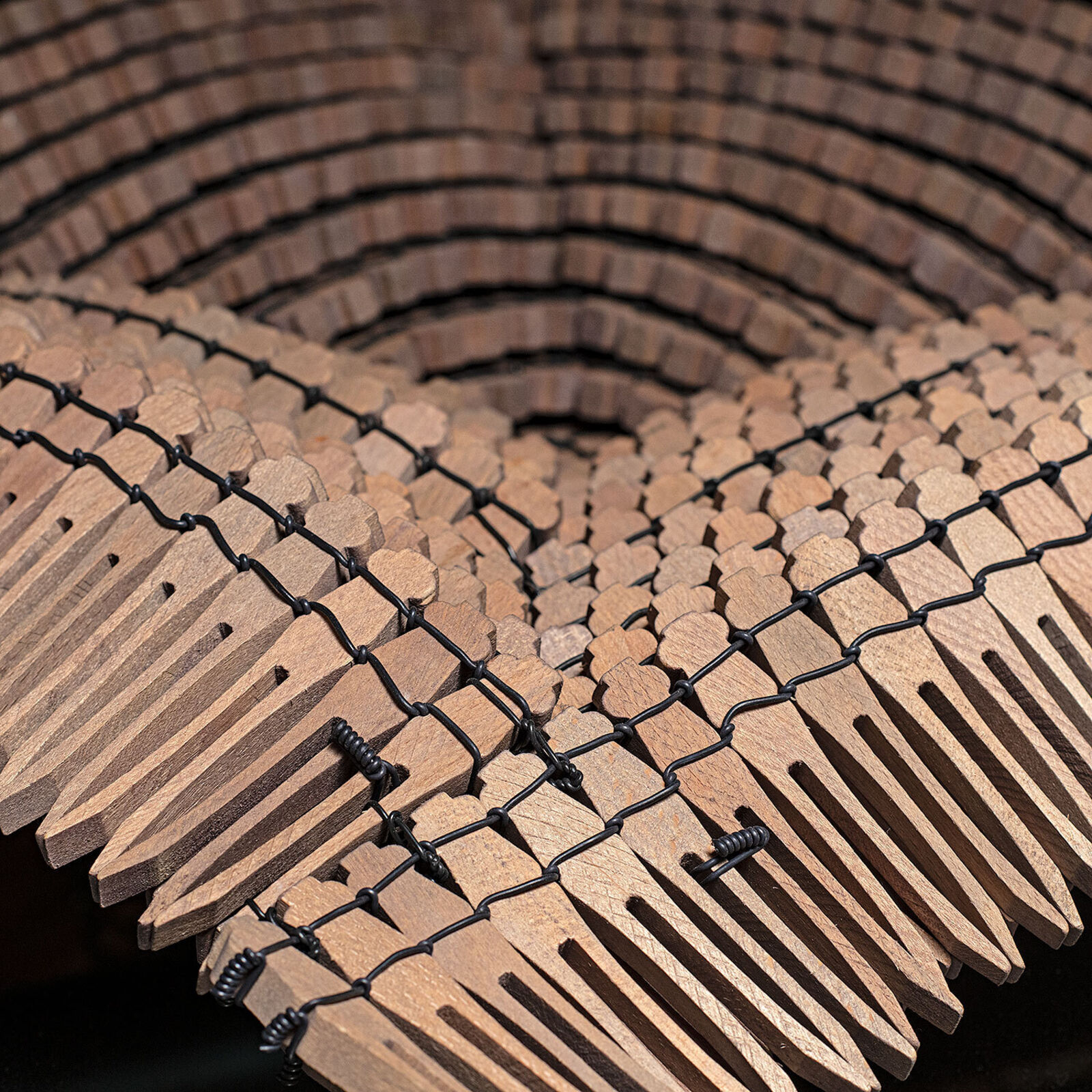A sculptural arrangement of wooden comb teeth forming a textured, curved surface on a dark table.