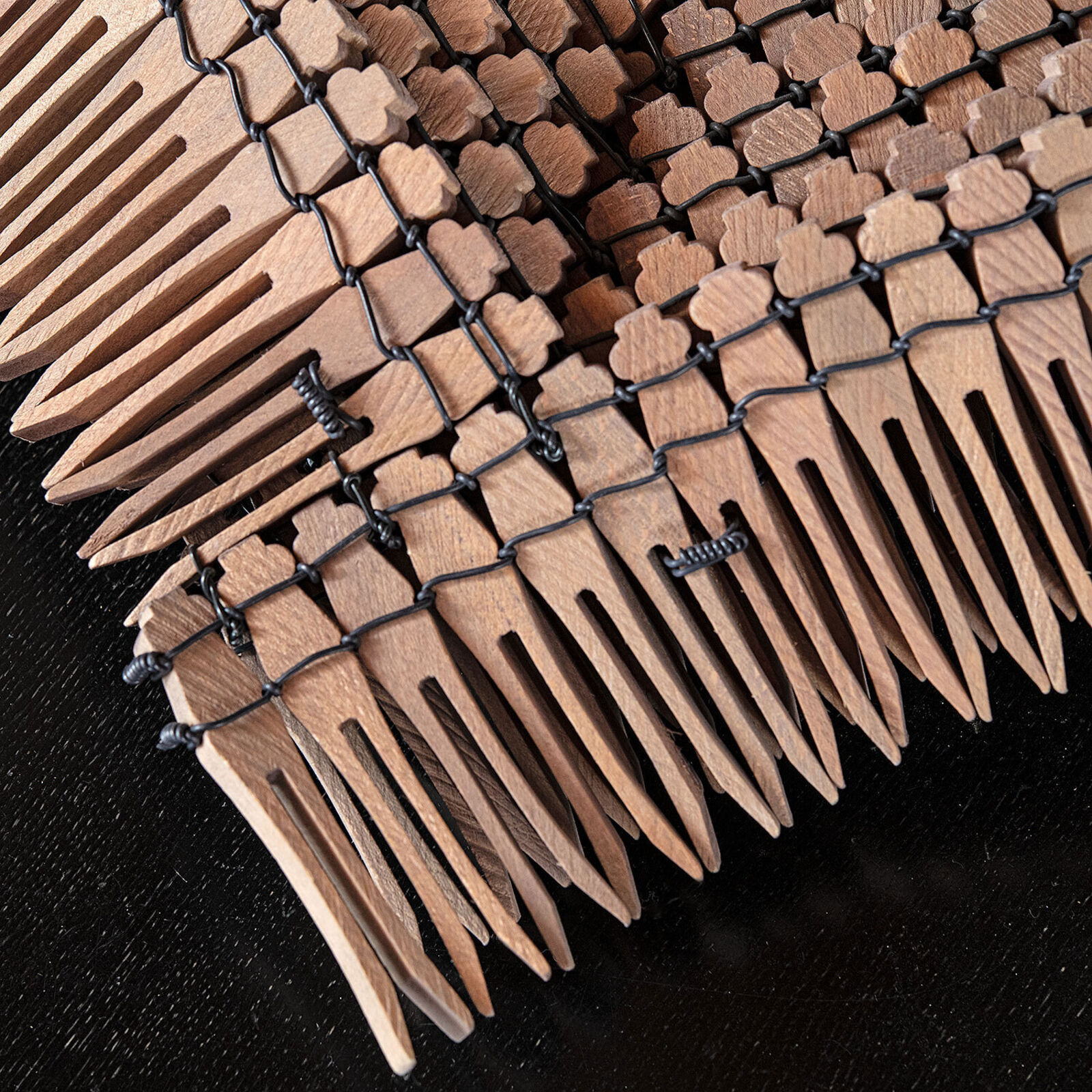 A sculptural arrangement of wooden comb teeth forming a textured, curved surface on a dark table.