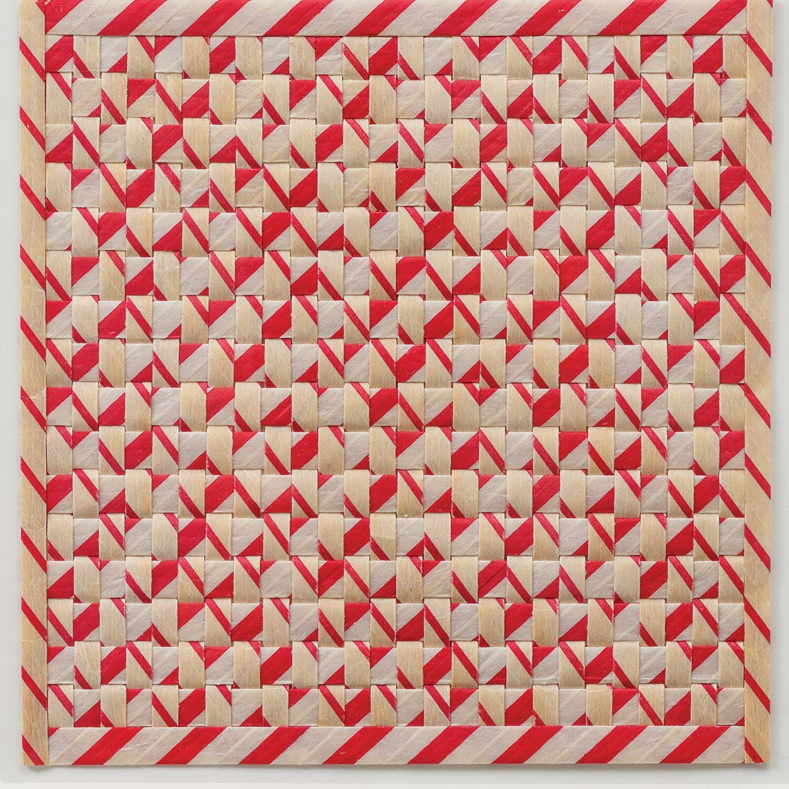 A framed textile artwork featuring a geometric red and cream pattern.
