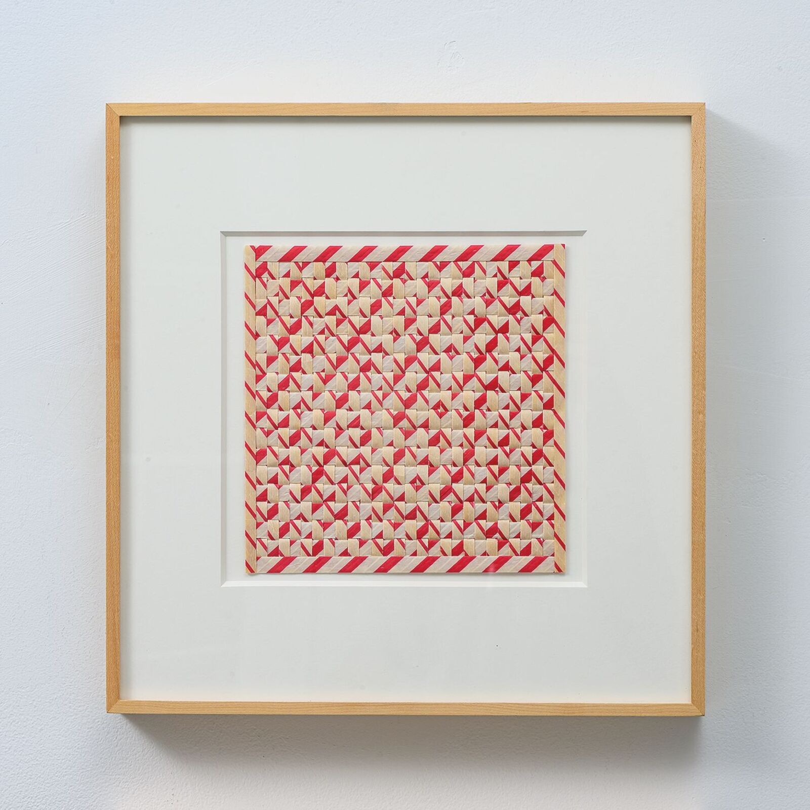A framed textile artwork featuring a geometric red and cream pattern.
