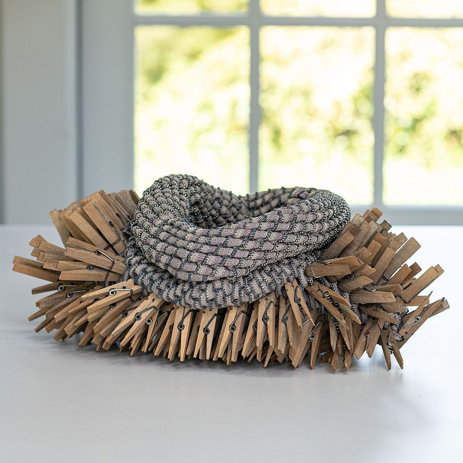 A necklace made out of clothes pins on a window sill.
