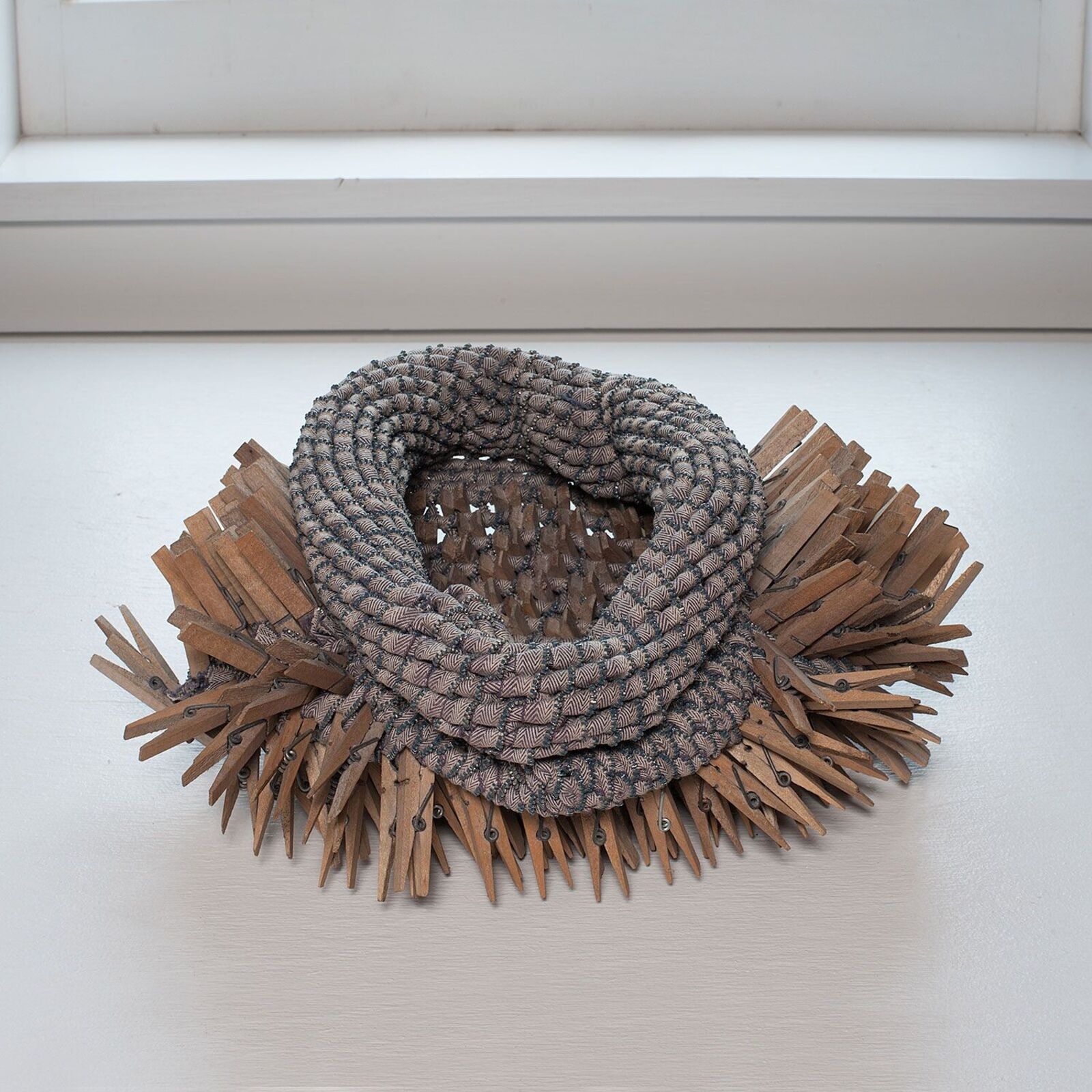 A necklace made out of clothes pins on a window sill.
