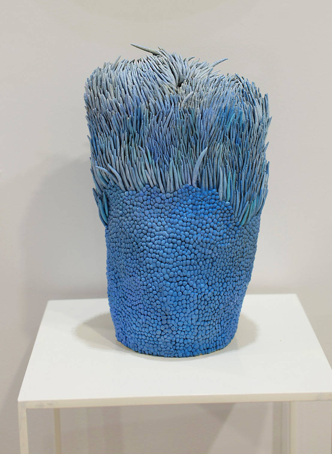 A sculptural piece featuring a textured blue base topped with spiky, grass-like elements.
