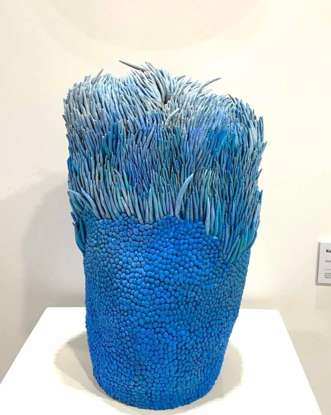 A sculptural piece featuring a textured blue base topped with spiky, grass-like elements.