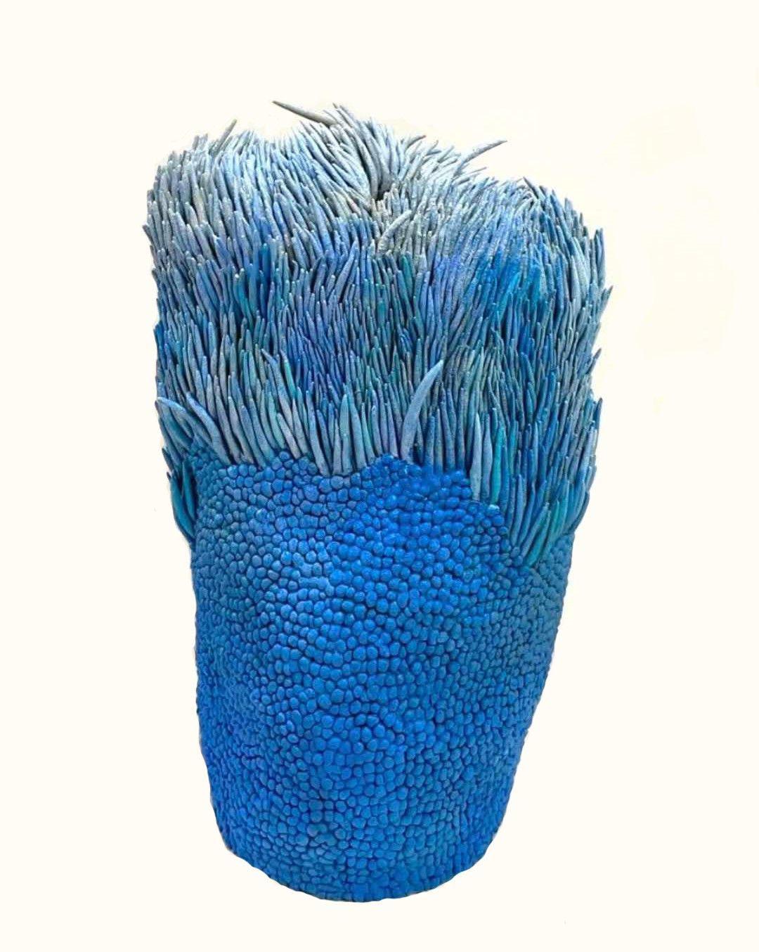 A sculptural piece featuring a textured blue base topped with spiky, grass-like elements.