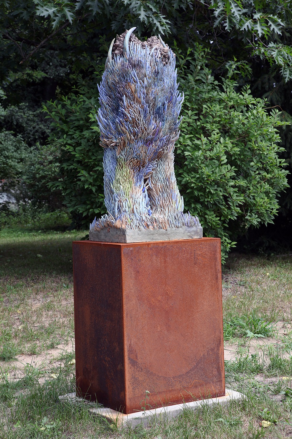 A sculpture of a bird sitting on top of a metal pedestal in the grass.