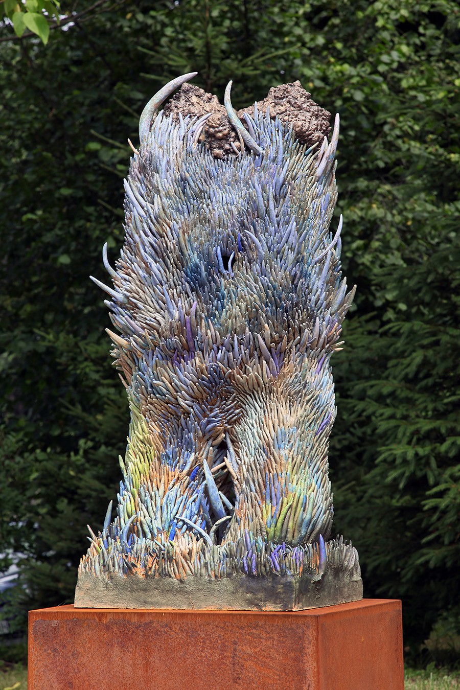 A sculpture of a bird sitting on top of a metal pedestal in the grass.