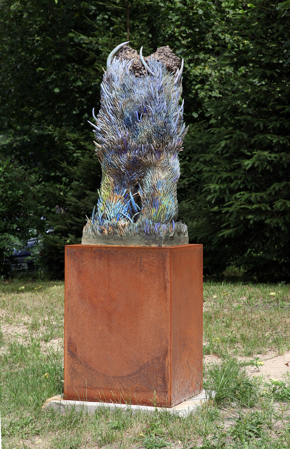 A sculpture of a bird sitting on top of a metal pedestal in the grass.