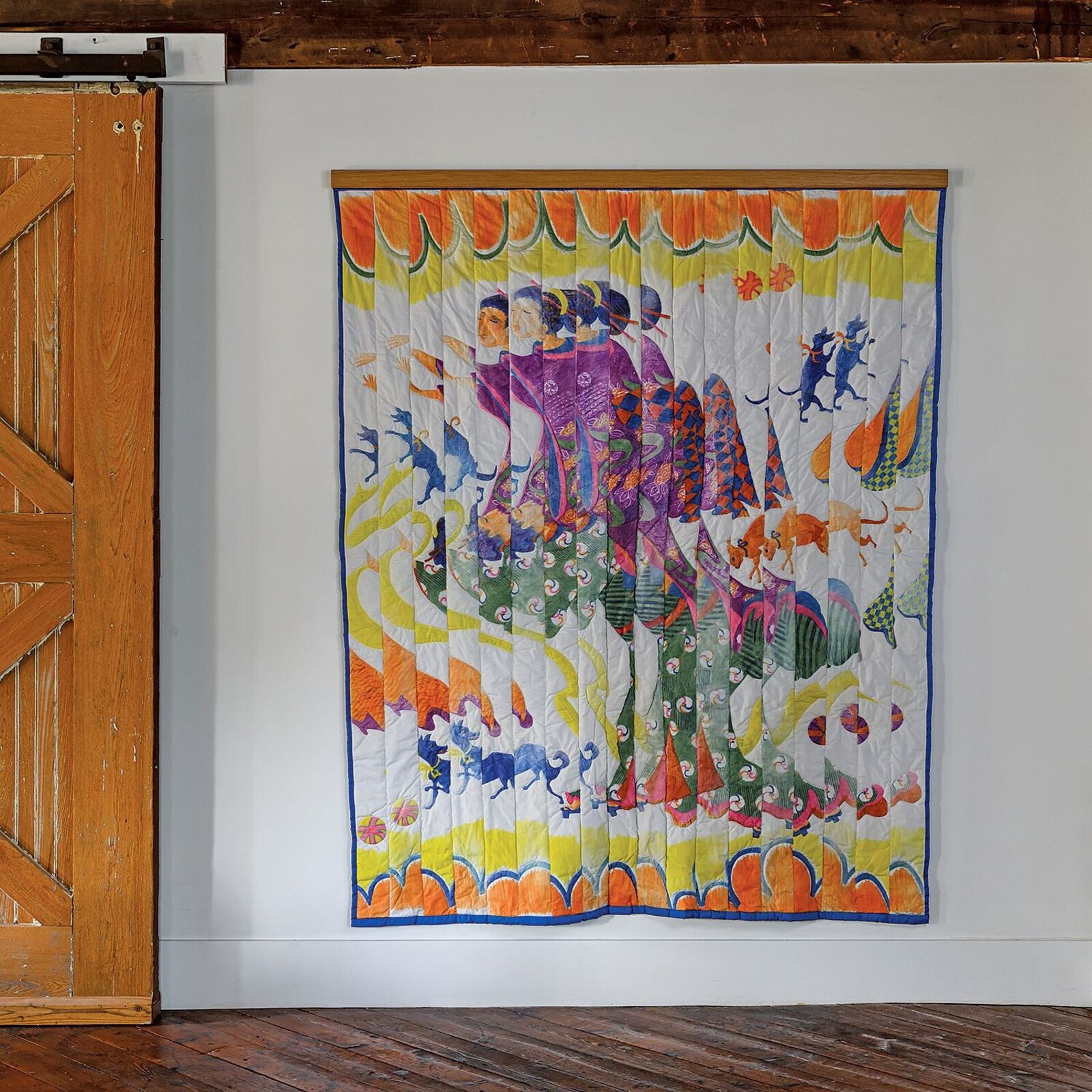 A colorful quilted tapestry featuring a whimsical scene of figures and animals against a bright, patterned background.