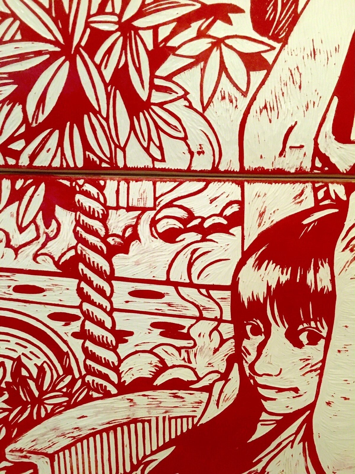 A red and white graphic print on three stacked skateboard decks displayed on a wooden stand.