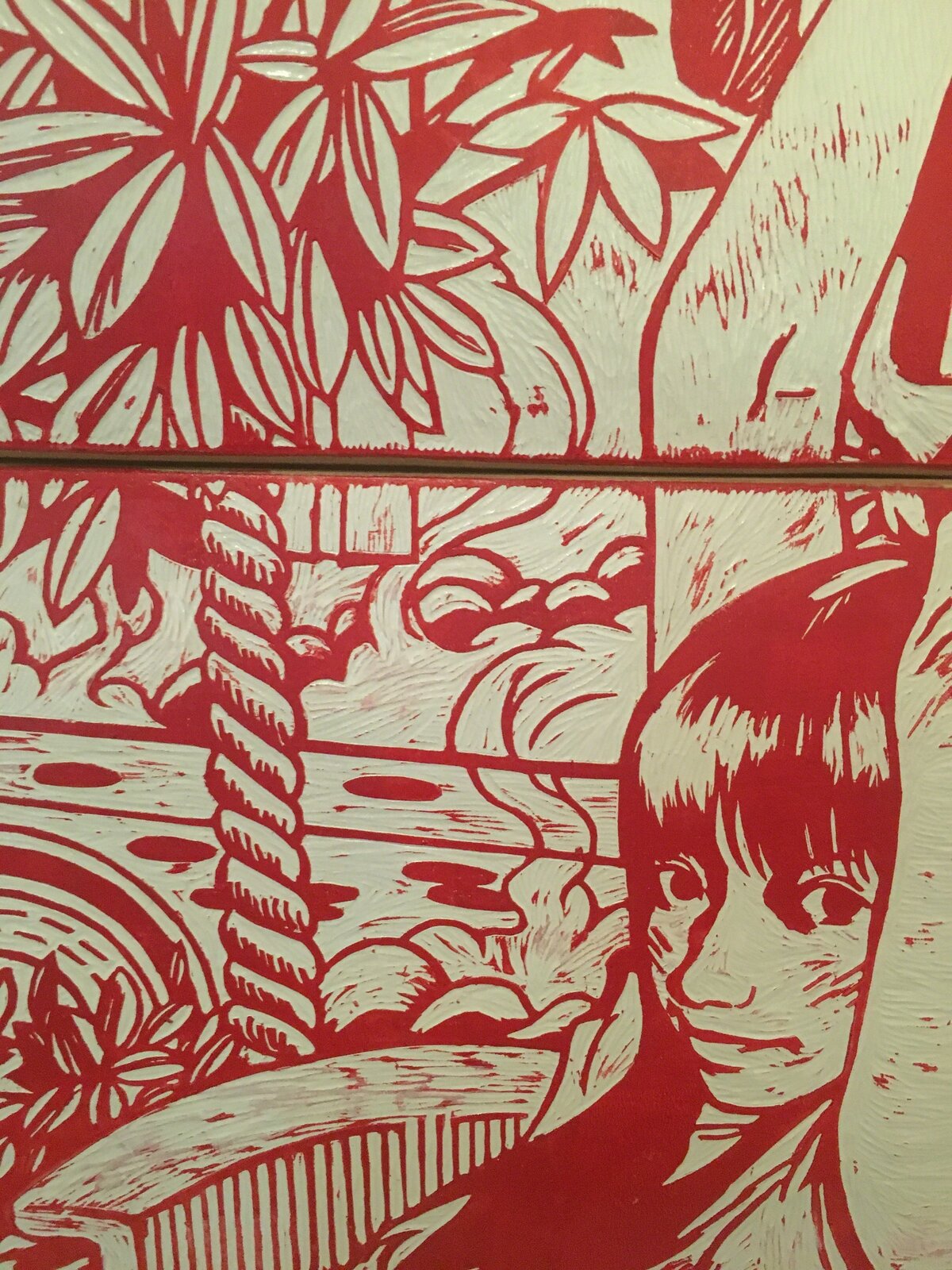 A red and white graphic print on three stacked skateboard decks displayed on a wooden stand.
