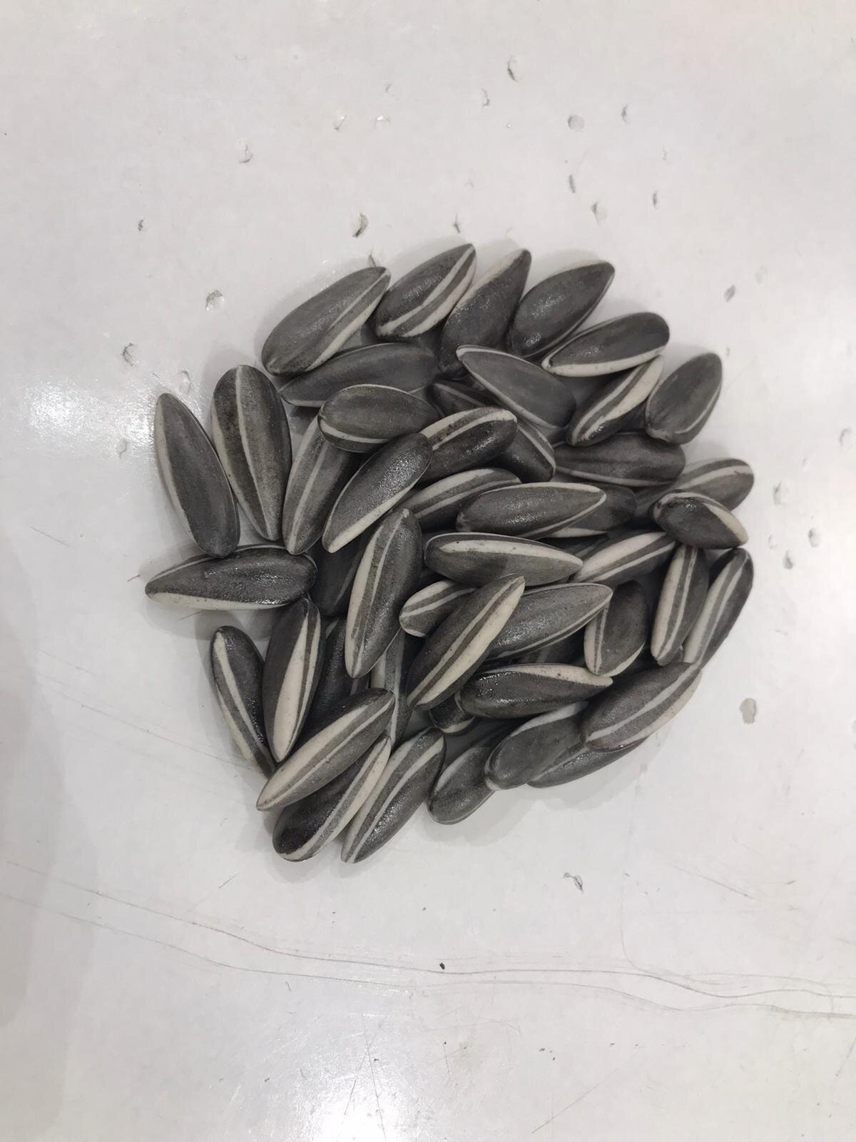 A top-down view of a pile of striped seeds on a white surface.