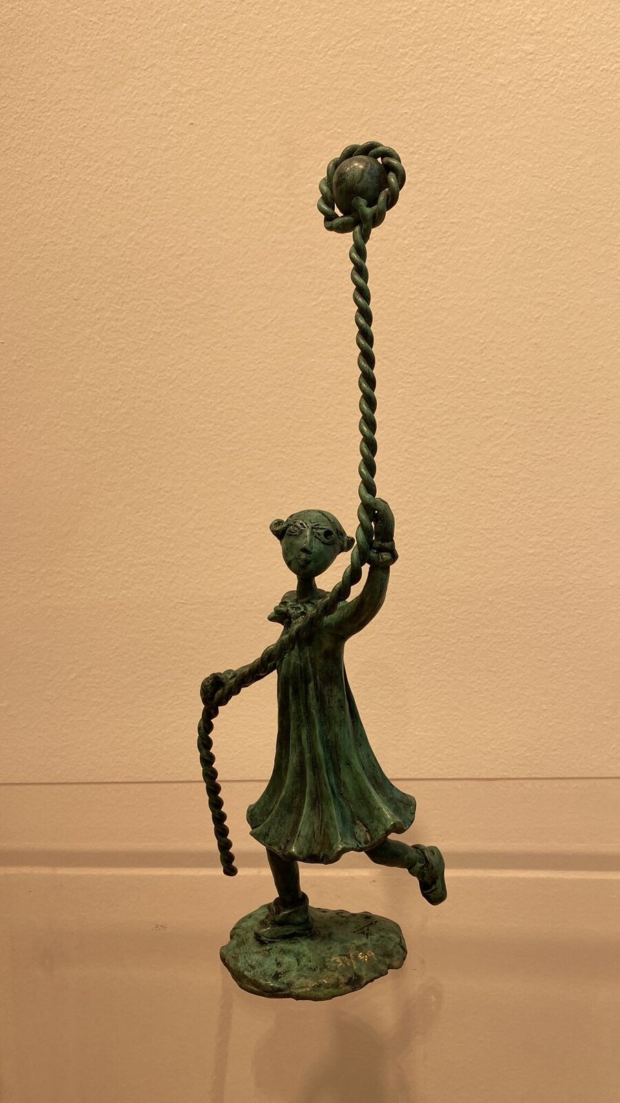 A bronze sculpture of a figure holding a long rope with a spherical object at the end.
