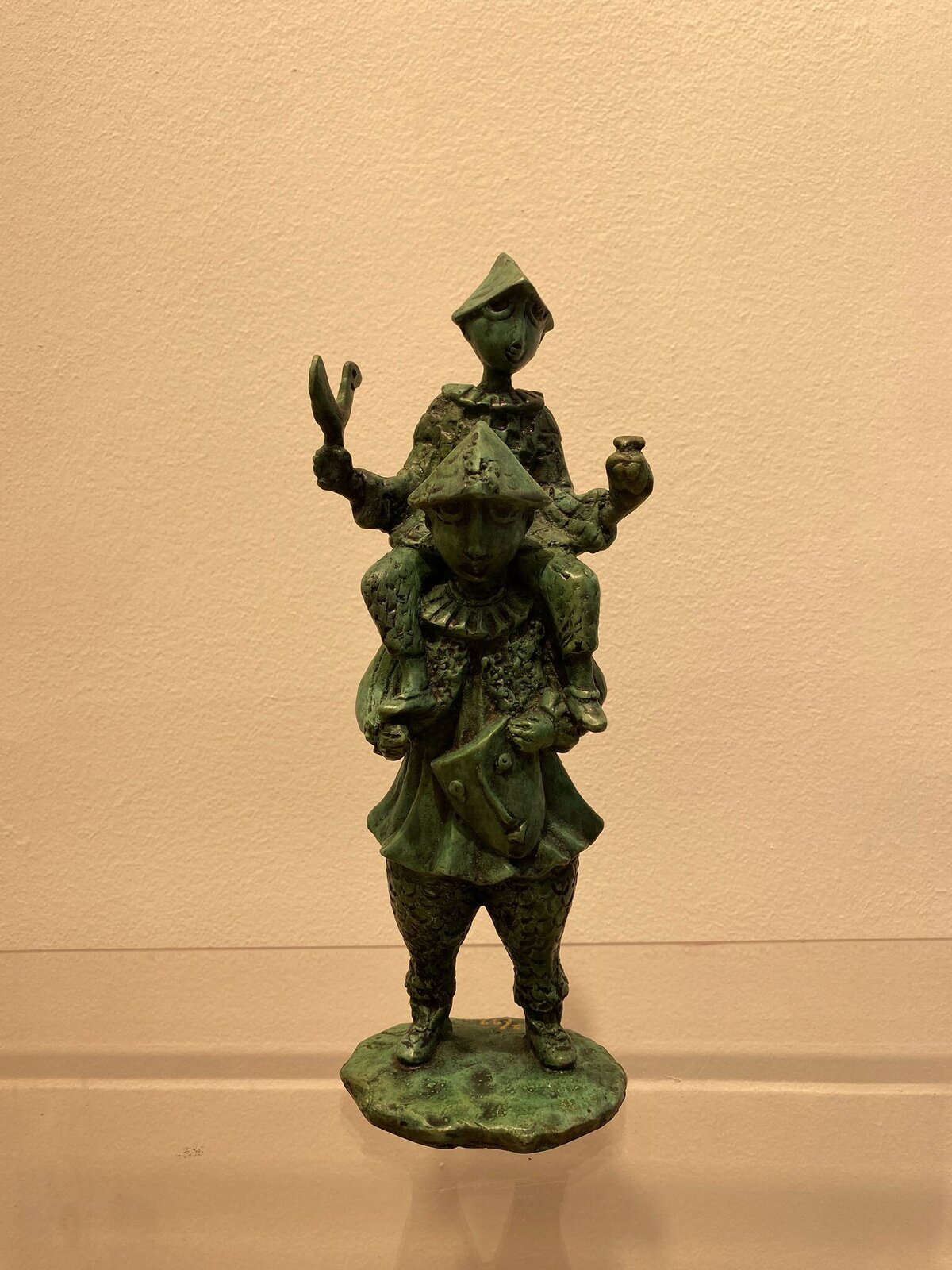 A green patinated bronze sculpture of a figure in armor viewed from behind, holding a small object and a sword.