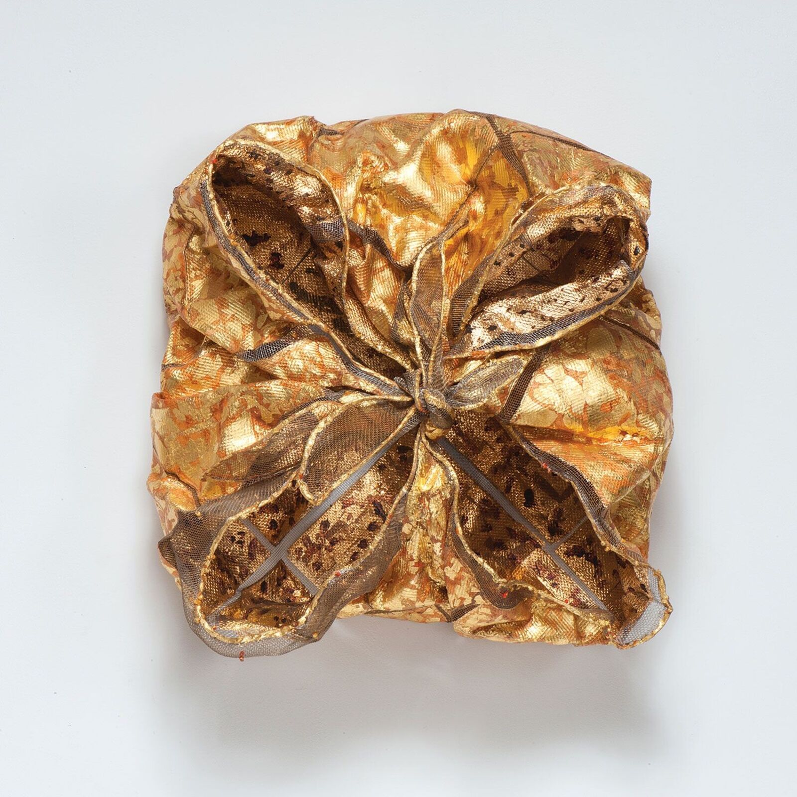 A golden, crumpled fabric sculpture resembling a gift box tied with ribbon.