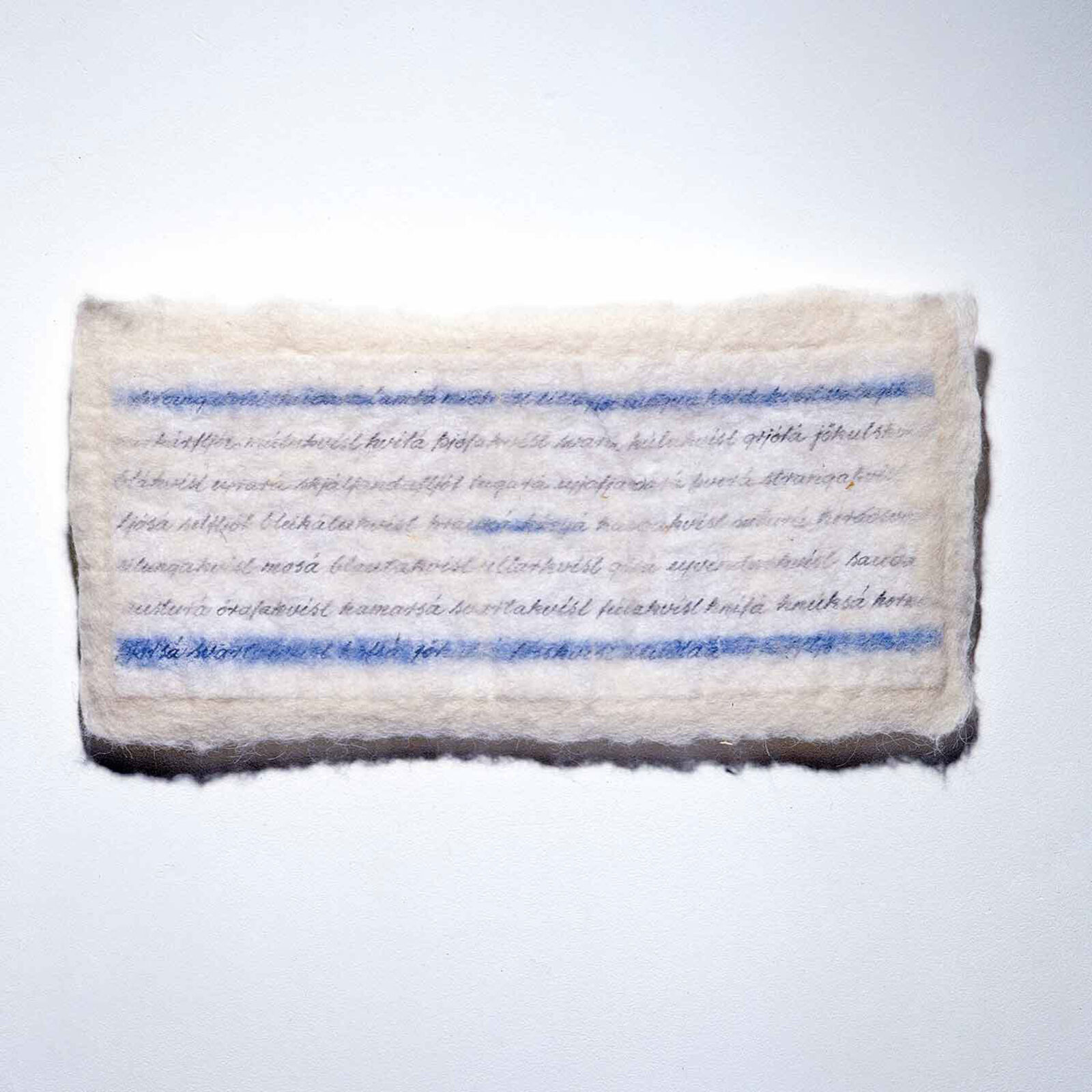 A minimalist textile artwork featuring blue and black script on a cream-colored felt, mounted on light wood.