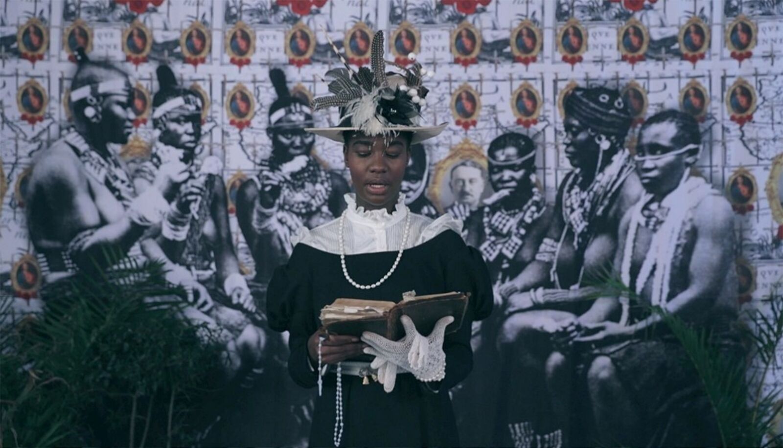 A woman in a black dress and hat holding a book.