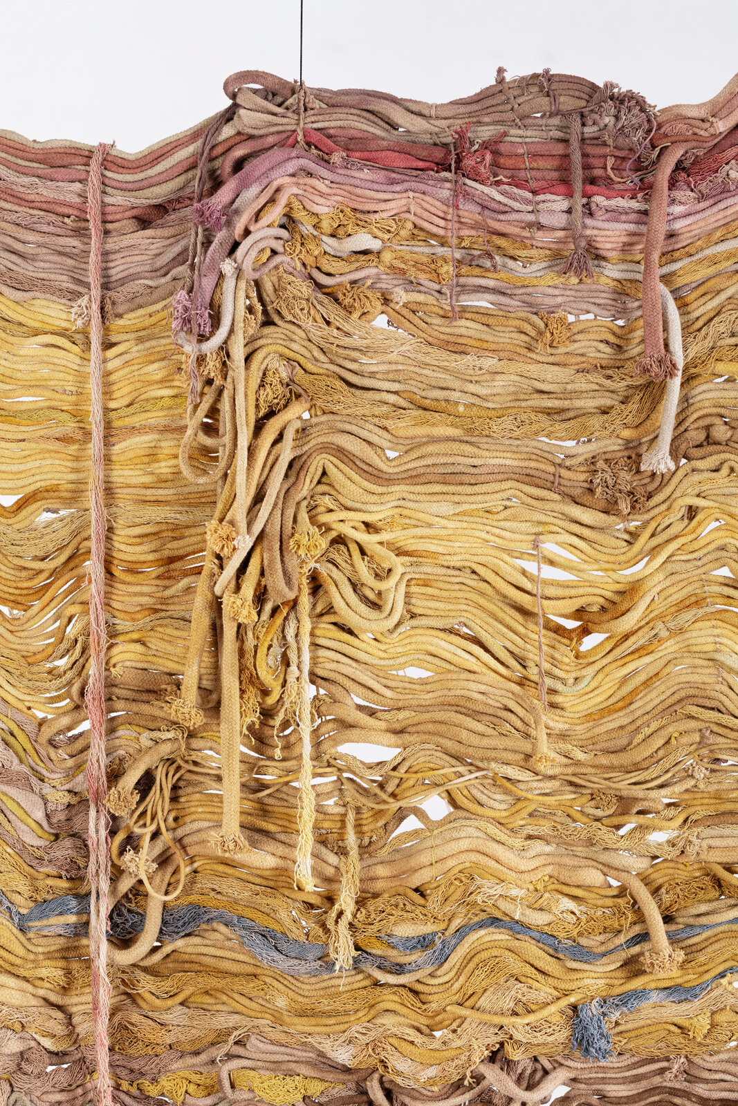 A textured textile artwork featuring layered, wavy threads in earthy tones.