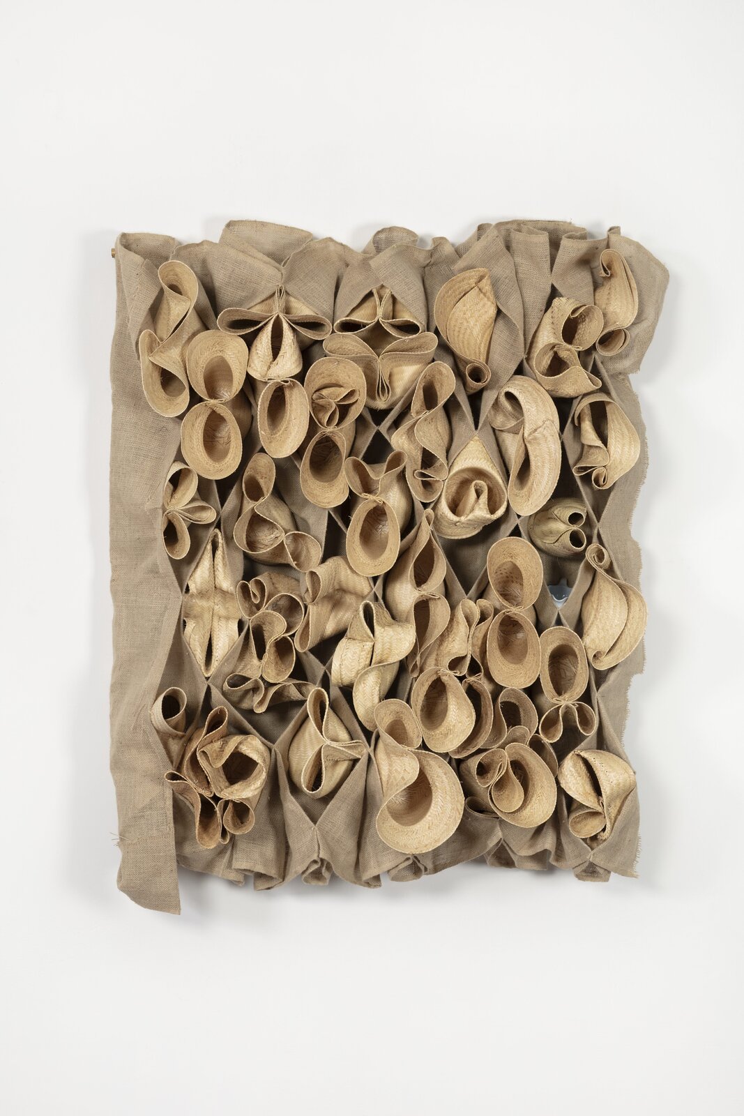 A textured relief sculpture featuring numerous rolled straw forms attached to a coarse fabric background.