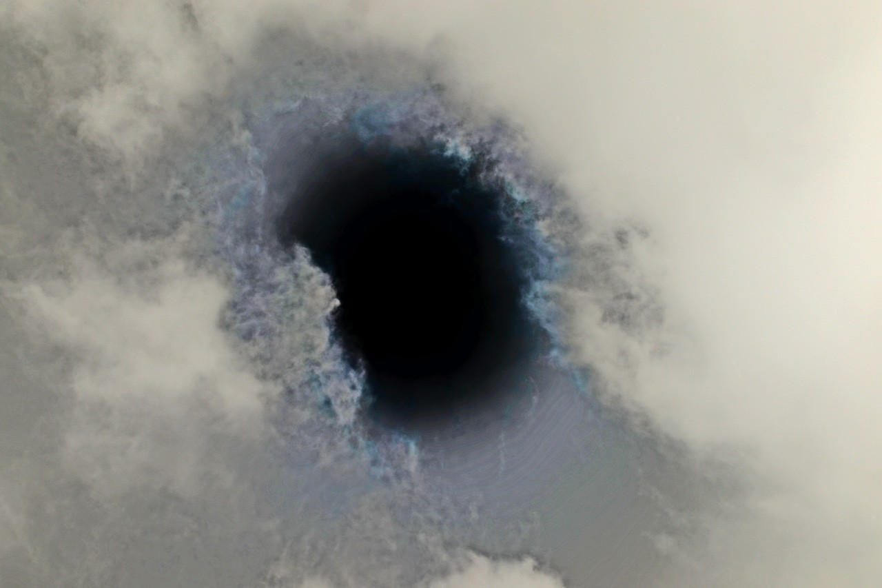 A surreal black hole surrounded by swirling blue and grey clouds.