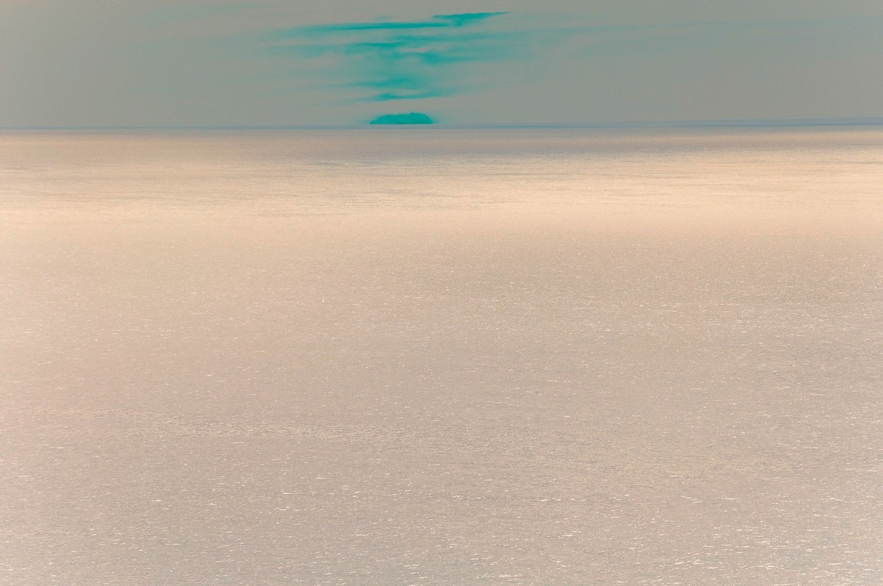 A serene seascape with a distant island under a soft, pastel sky.