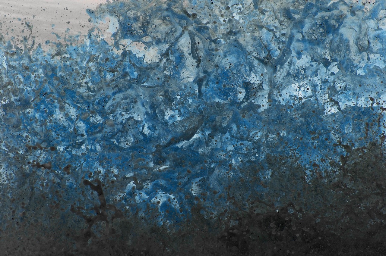 An abstract composition of splattered blue and grey paint on a textured surface.