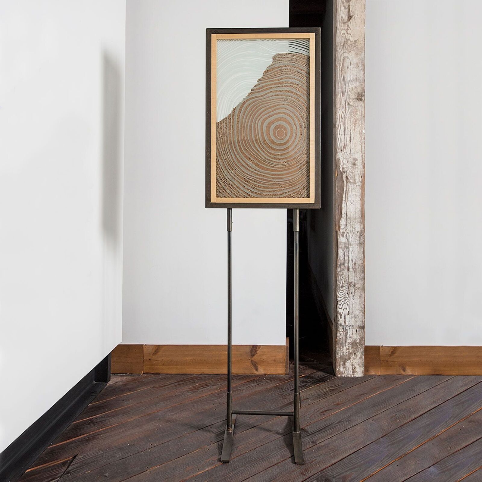A framed artwork of concentric circles displayed on a metal easel in a minimalist interior.