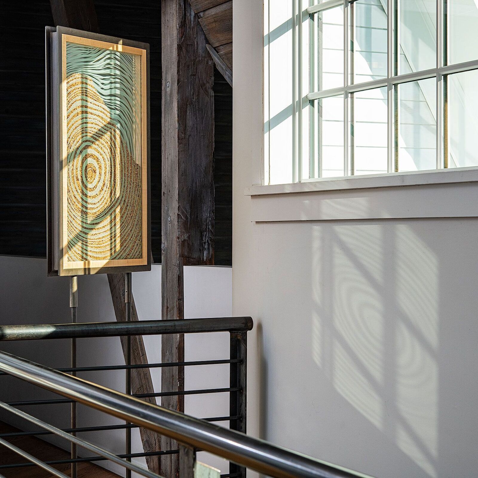 A framed artwork of concentric circles displayed on a metal easel in a minimalist interior.