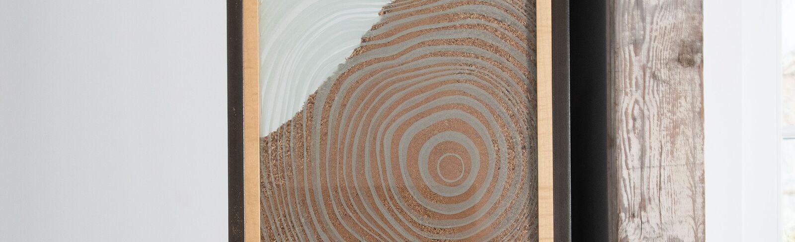 A framed artwork of concentric circles displayed on a metal easel in a minimalist interior.