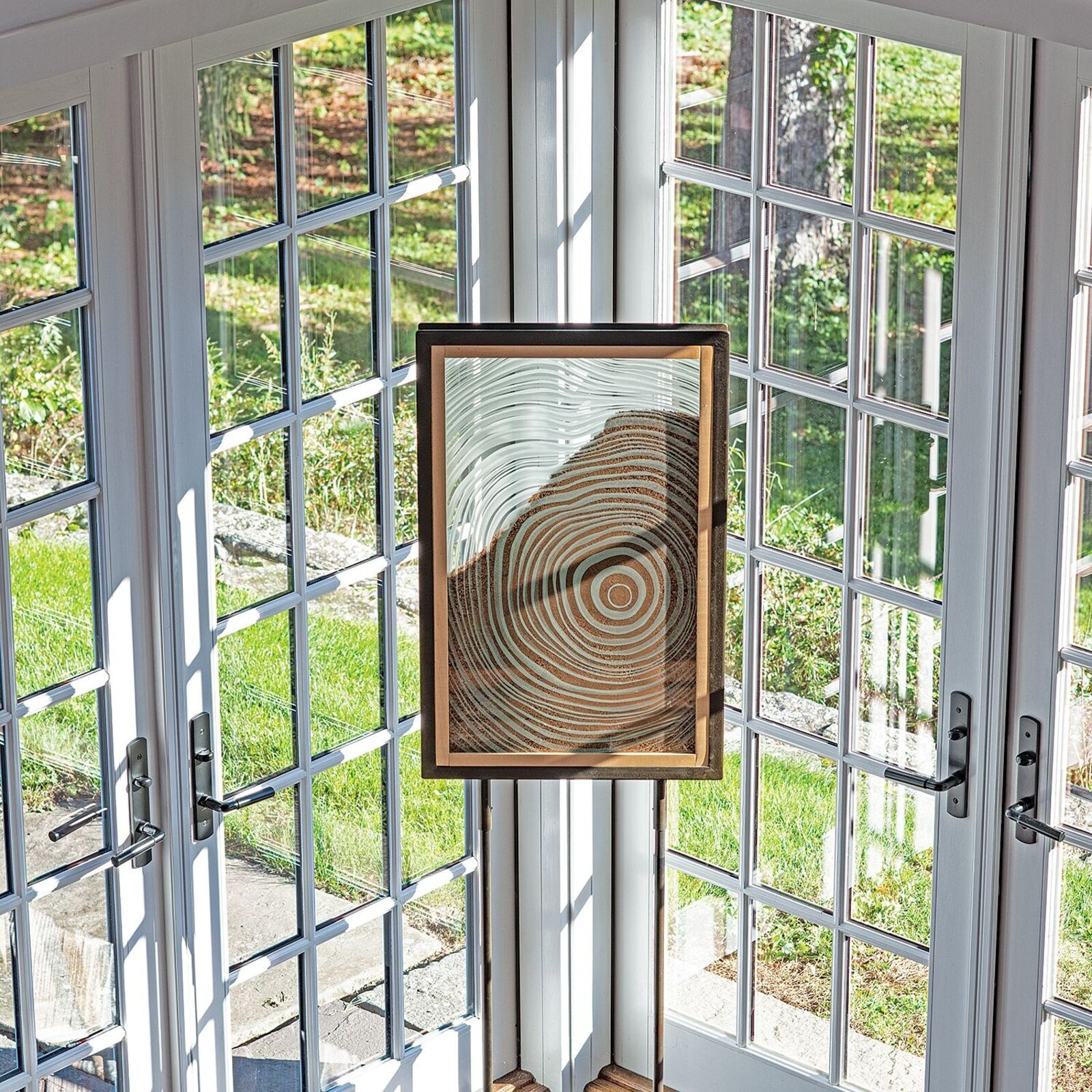 A framed artwork of concentric circles displayed on a metal easel in a minimalist interior.