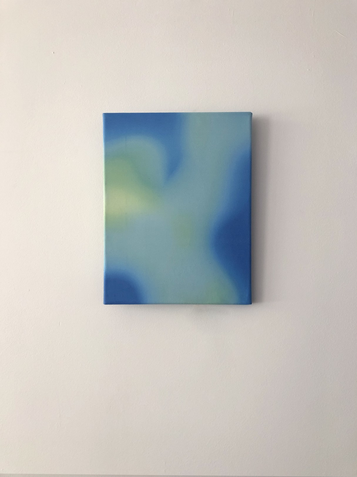 A minimalist abstract painting featuring soft blue and green gradients on a white wall.