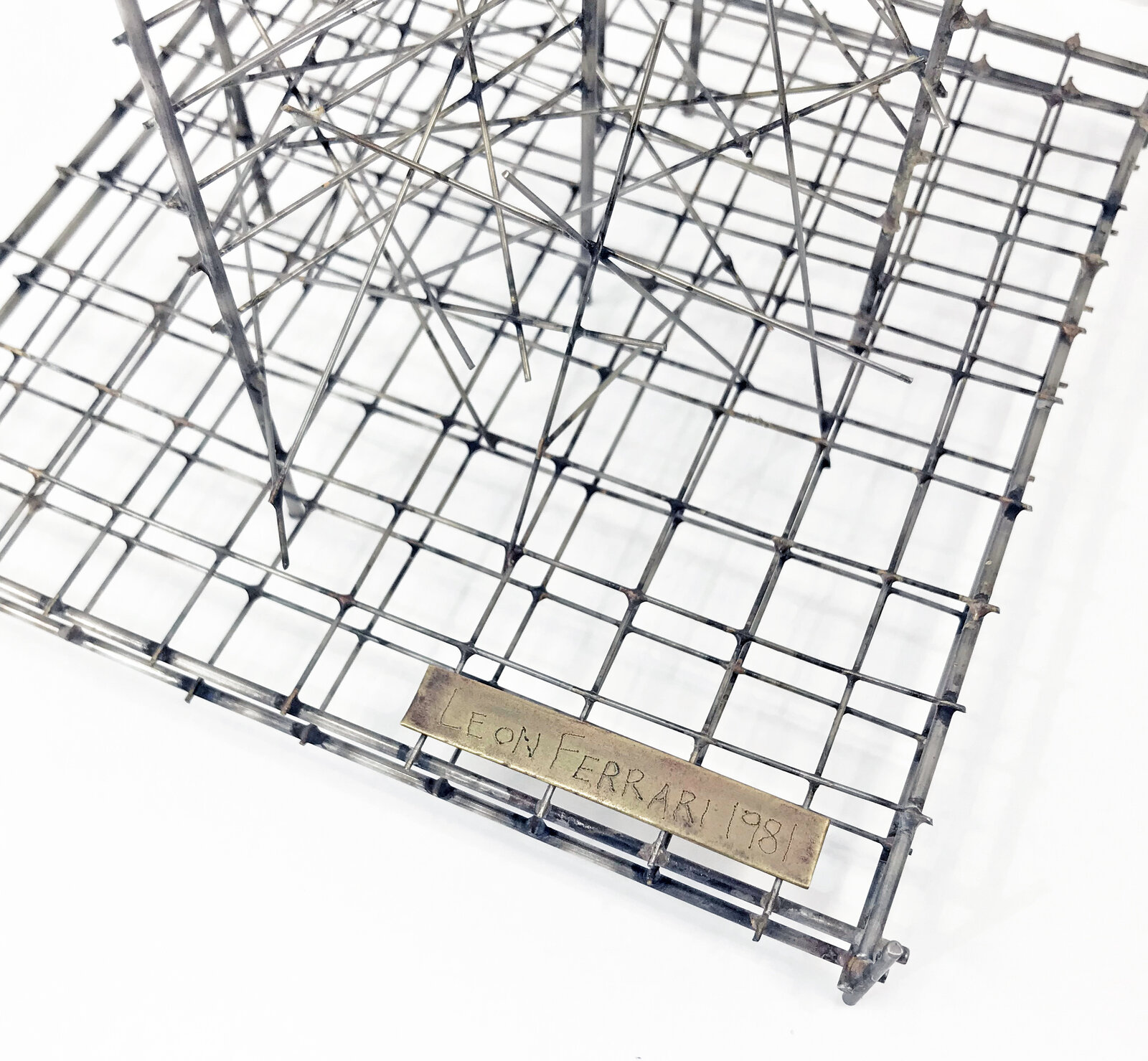 A tall, minimalist sculpture featuring a grid-like base and vertical wire structures against a stark white background.