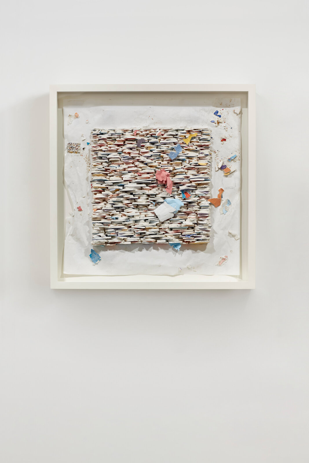 A framed relief sculpture featuring a textured, layered surface with scattered colorful fragments.