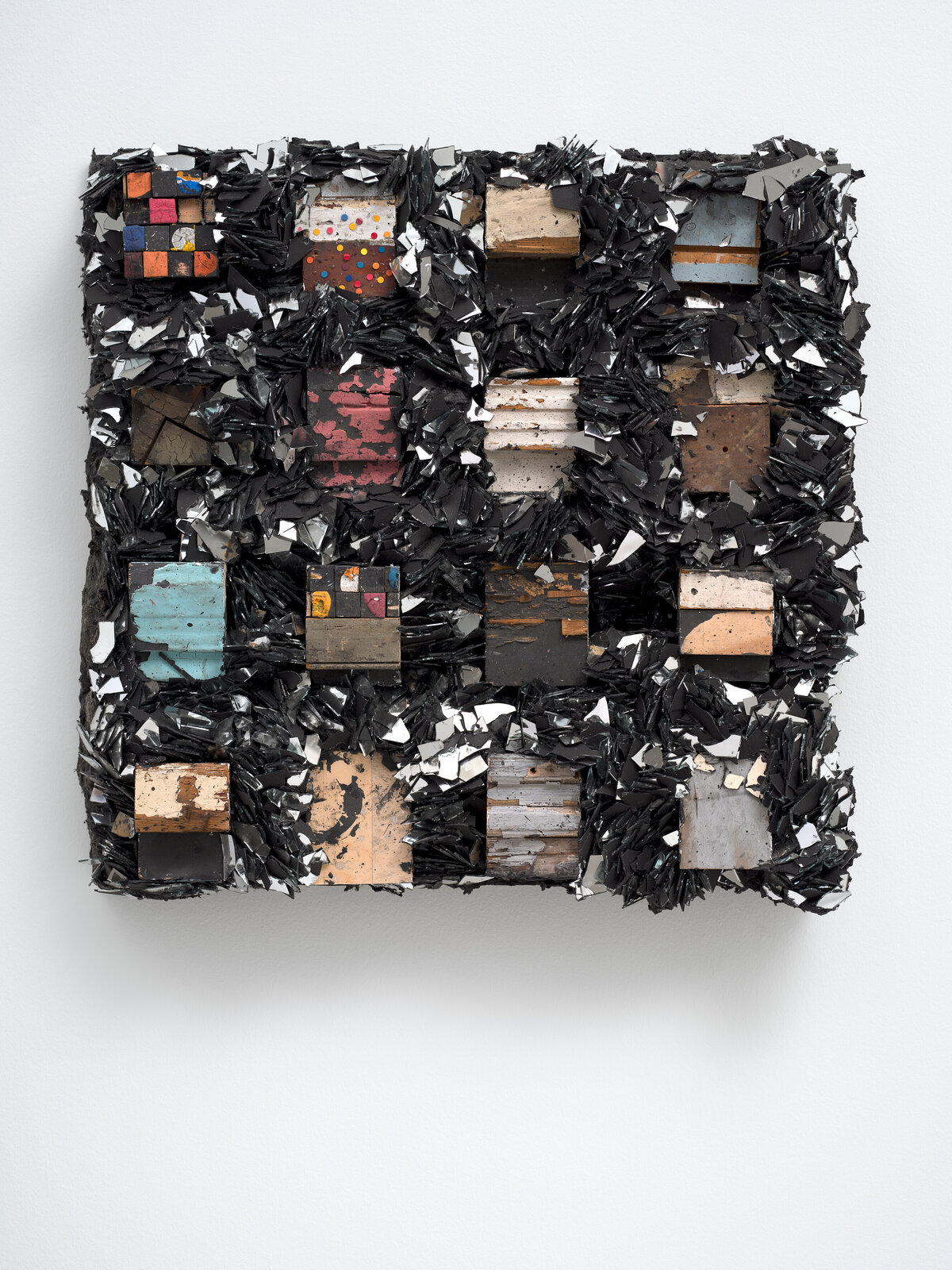 A mixed-media relief sculpture featuring a grid of weathered wooden blocks surrounded by jagged shards of black material.