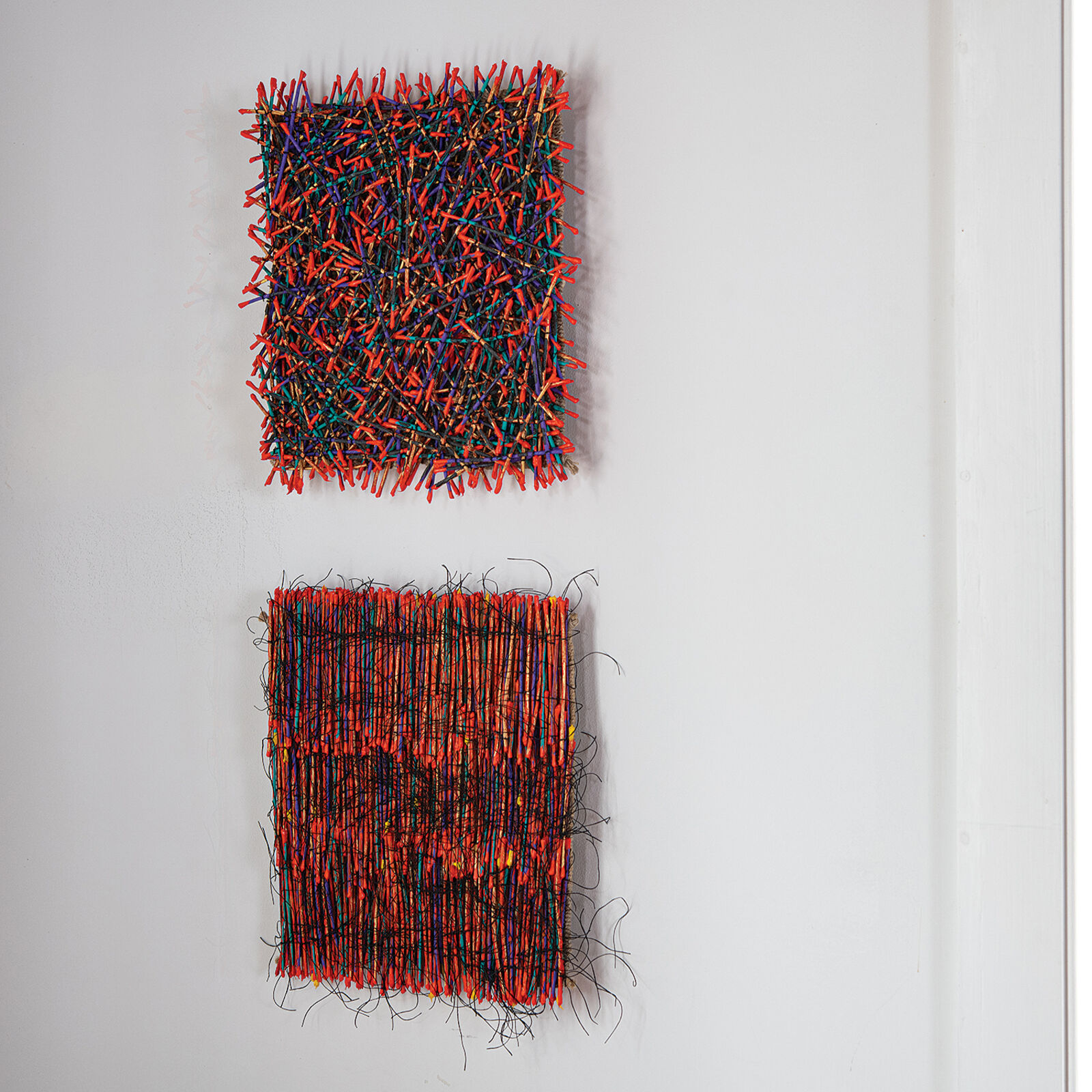 A vibrant textile artwork featuring a dense weave of orange threads interlaced with black and multicolored fibers.