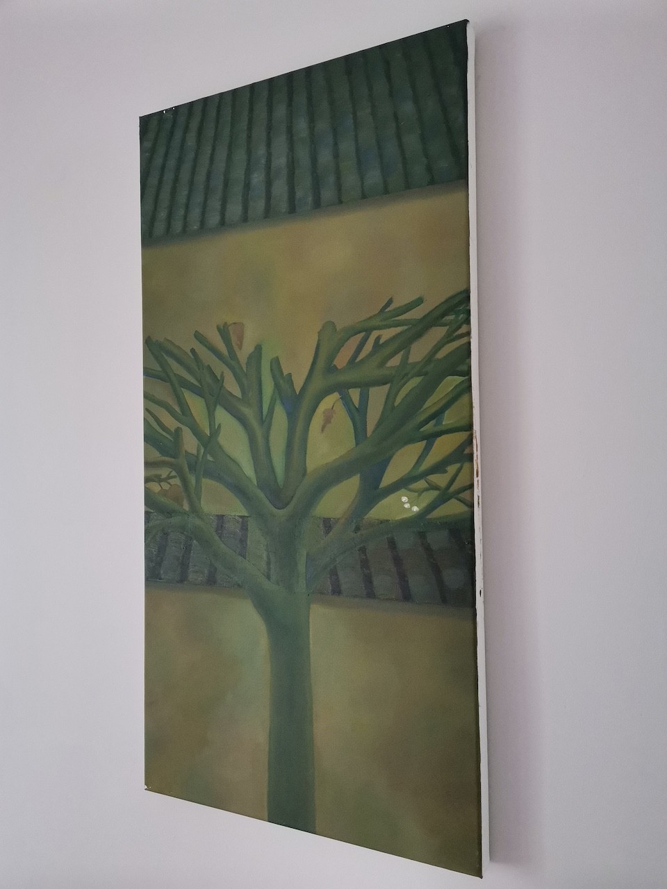 "A vertical painting of a leafless tree against a muted yellow wall with a dark tiled roof above."