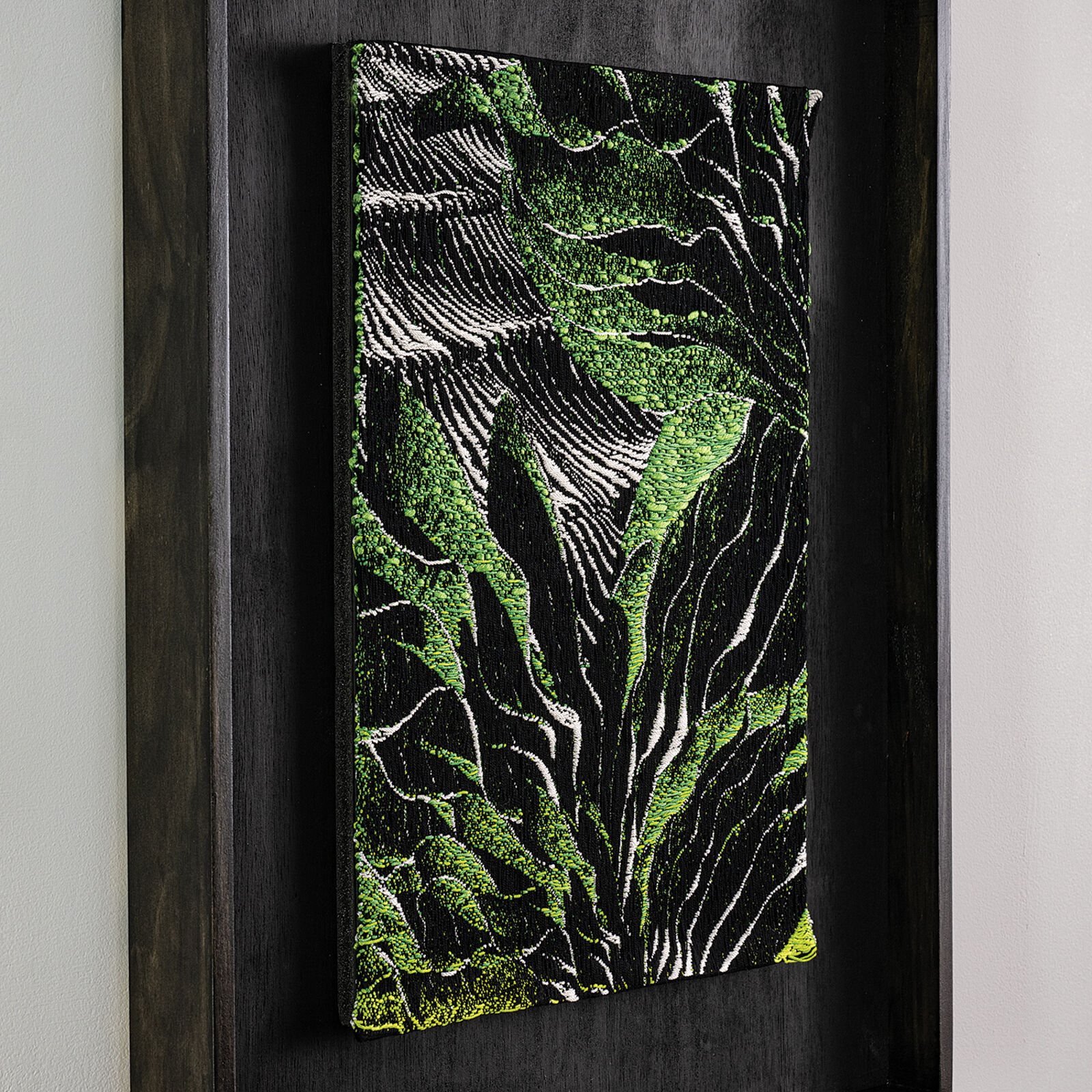 A framed textile artwork featuring a vibrant green and black abstract pattern.