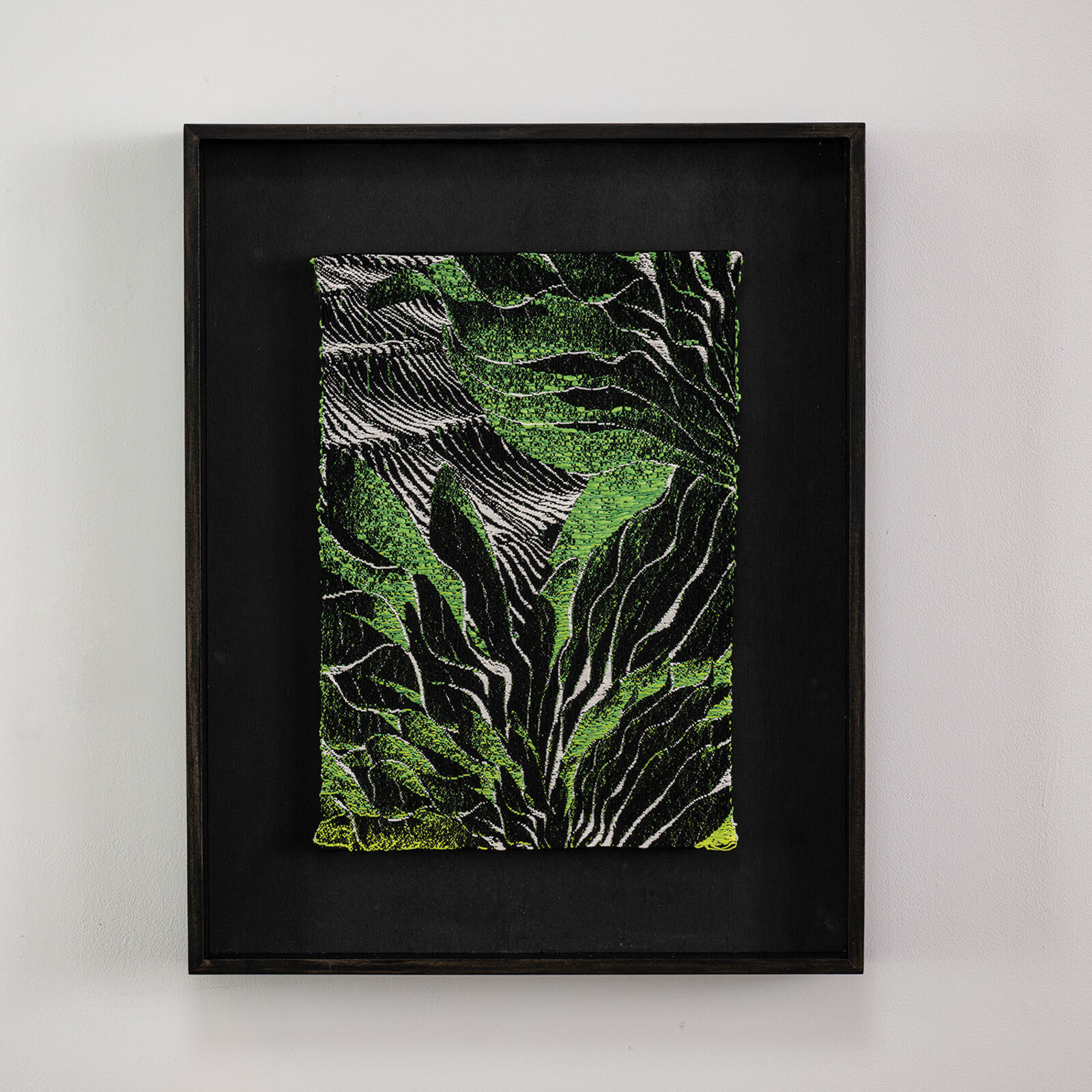A framed textile artwork featuring a vibrant green and black abstract pattern.
