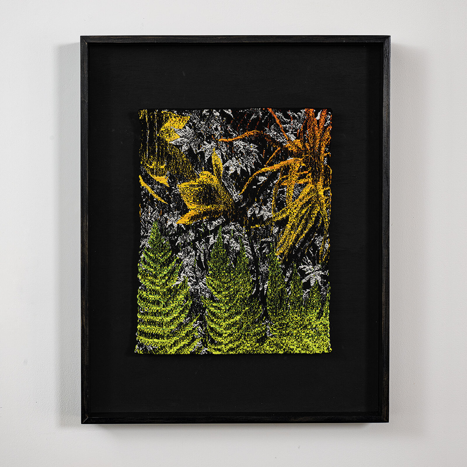 A framed textile artwork featuring a dense, textured forest scene with vibrant green ferns and yellow foliage against a dark background.