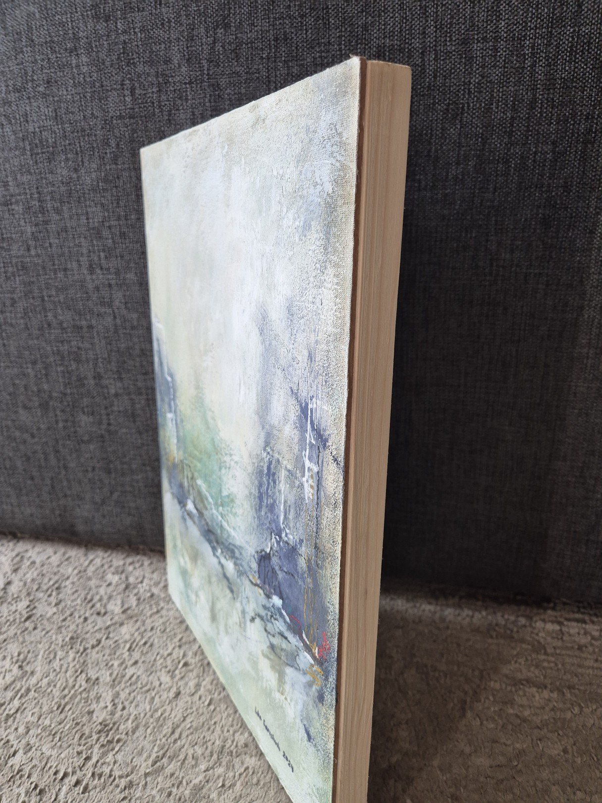 An abstract textured painting featuring a muted palette of grey, blue, and yellow with visible brushstrokes.