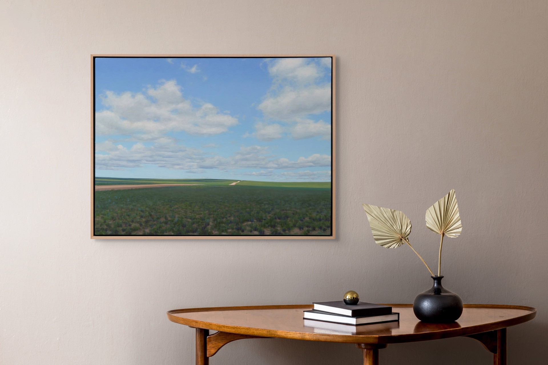 A vast landscape painting of rolling green fields under a blue sky filled with fluffy white clouds.