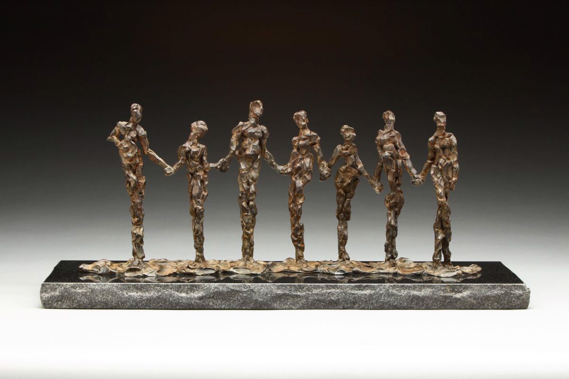 A bronze sculpture of seven hand-holding figures standing on a dark marble base.