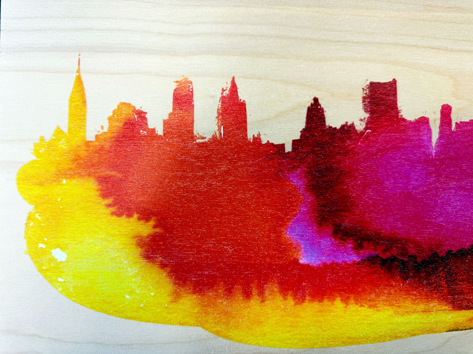 A watercolor painting of a city skyline on a wooden surface.