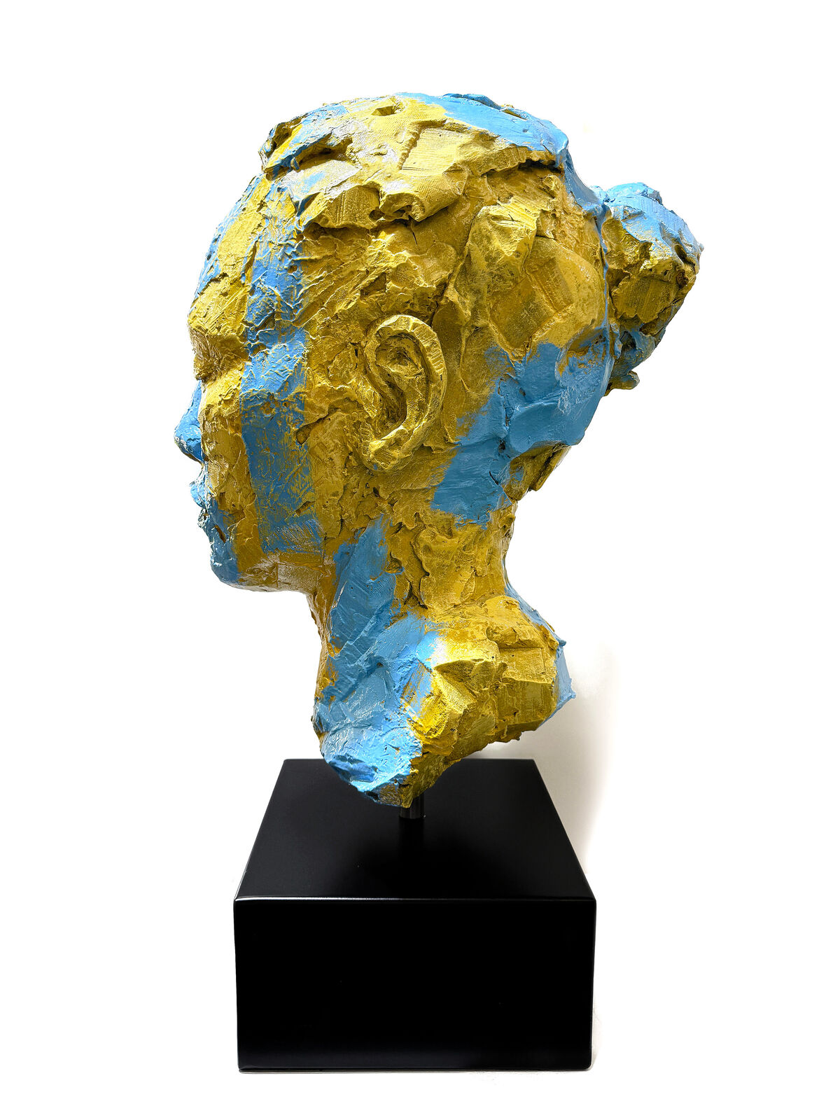 A yellow and blue sculpture of a woman's face on a black stand.