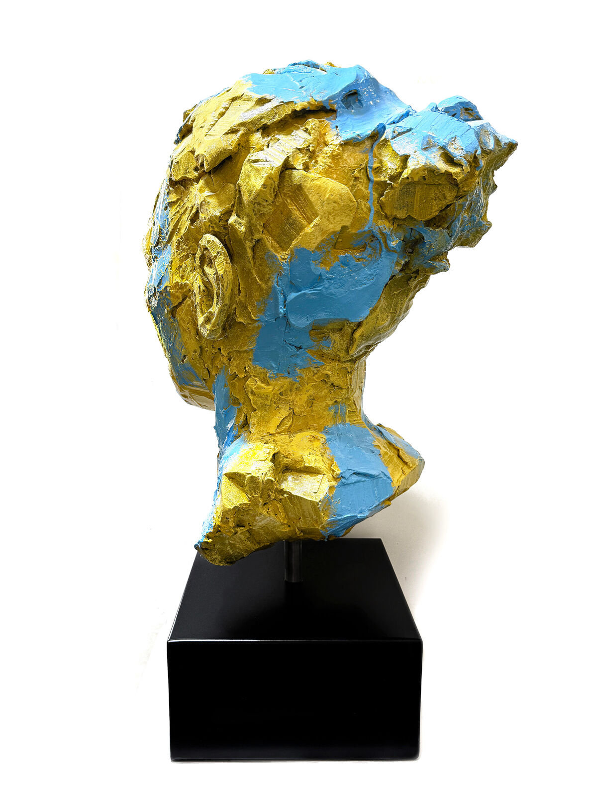 A yellow and blue sculpture of a woman's face on a black stand.