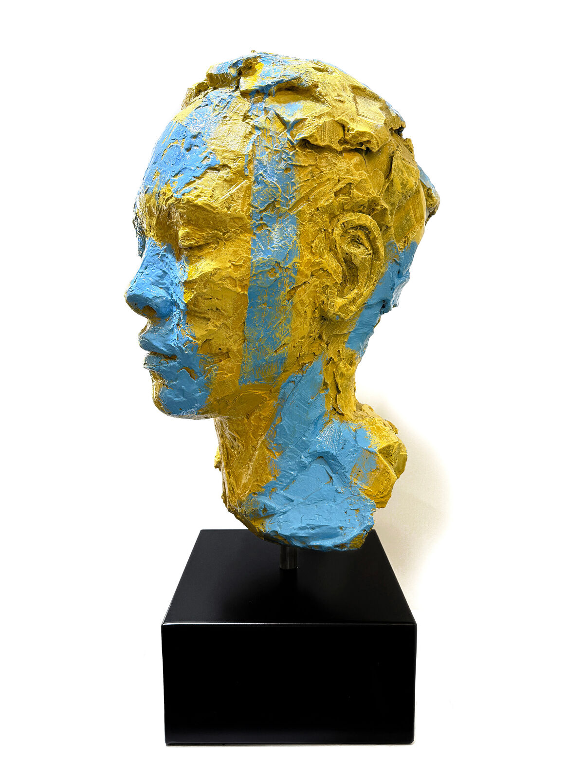 A yellow and blue sculpture of a woman's face on a black stand.